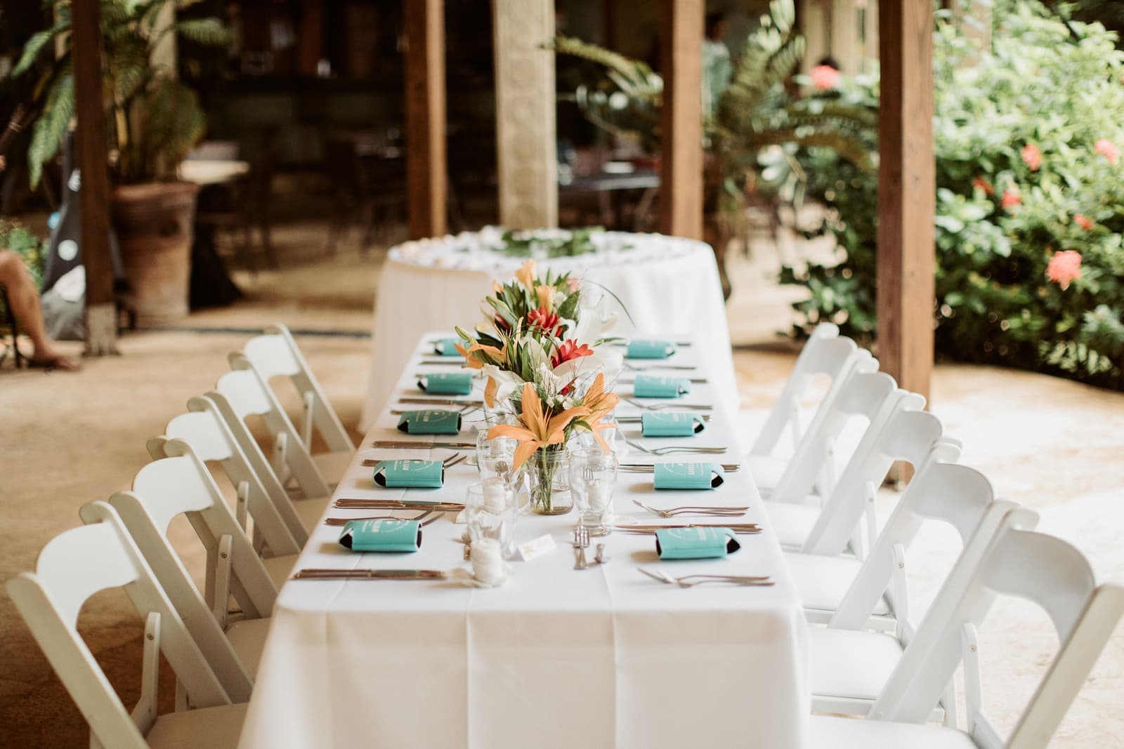 A beautifully arranged dining table with white chairs, decorated with flowers and turquoise napkins in a tropical setting.