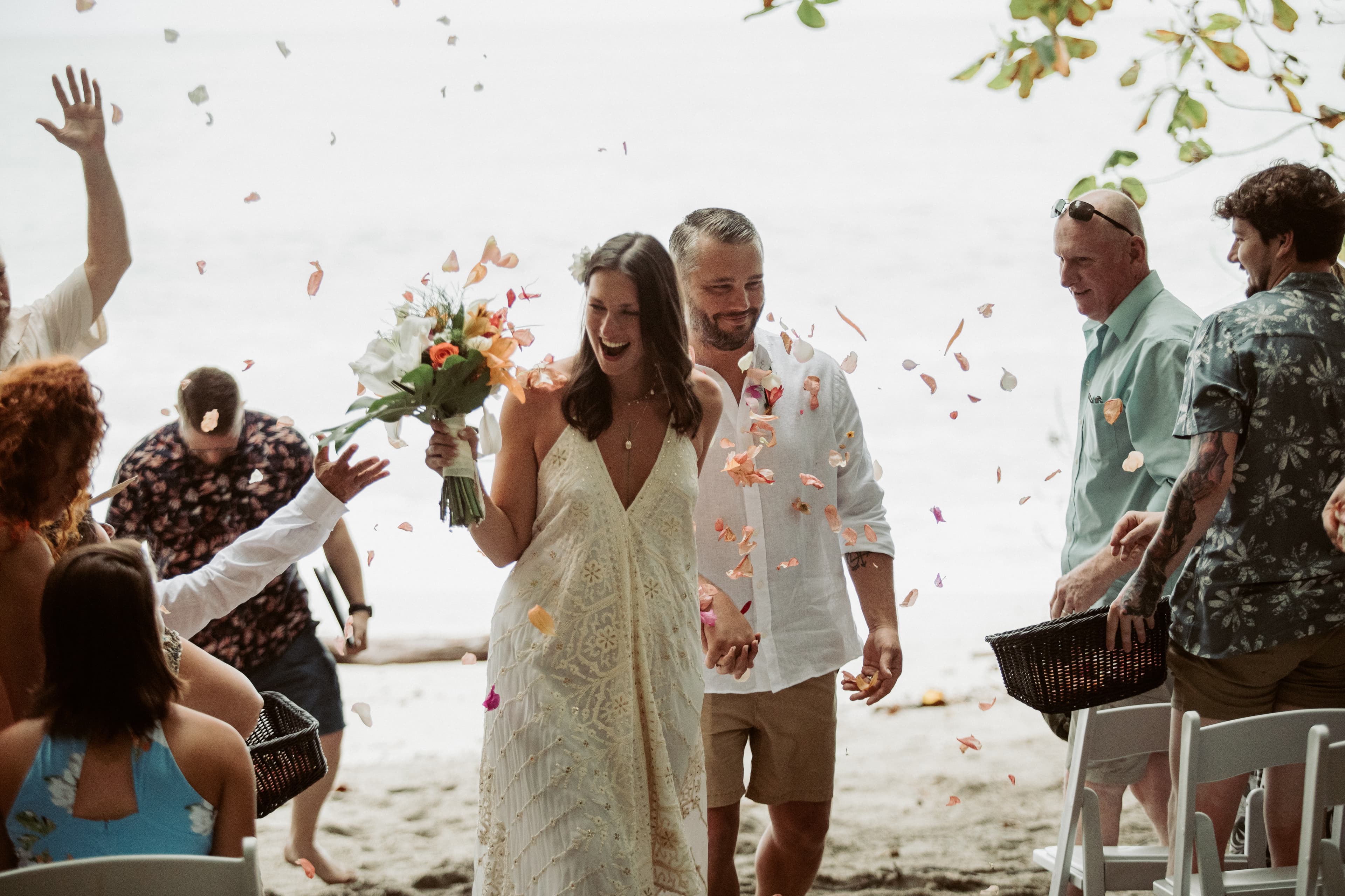 Wedding guests tossing flower petals at a bridge and groom at a beachfront ceremony