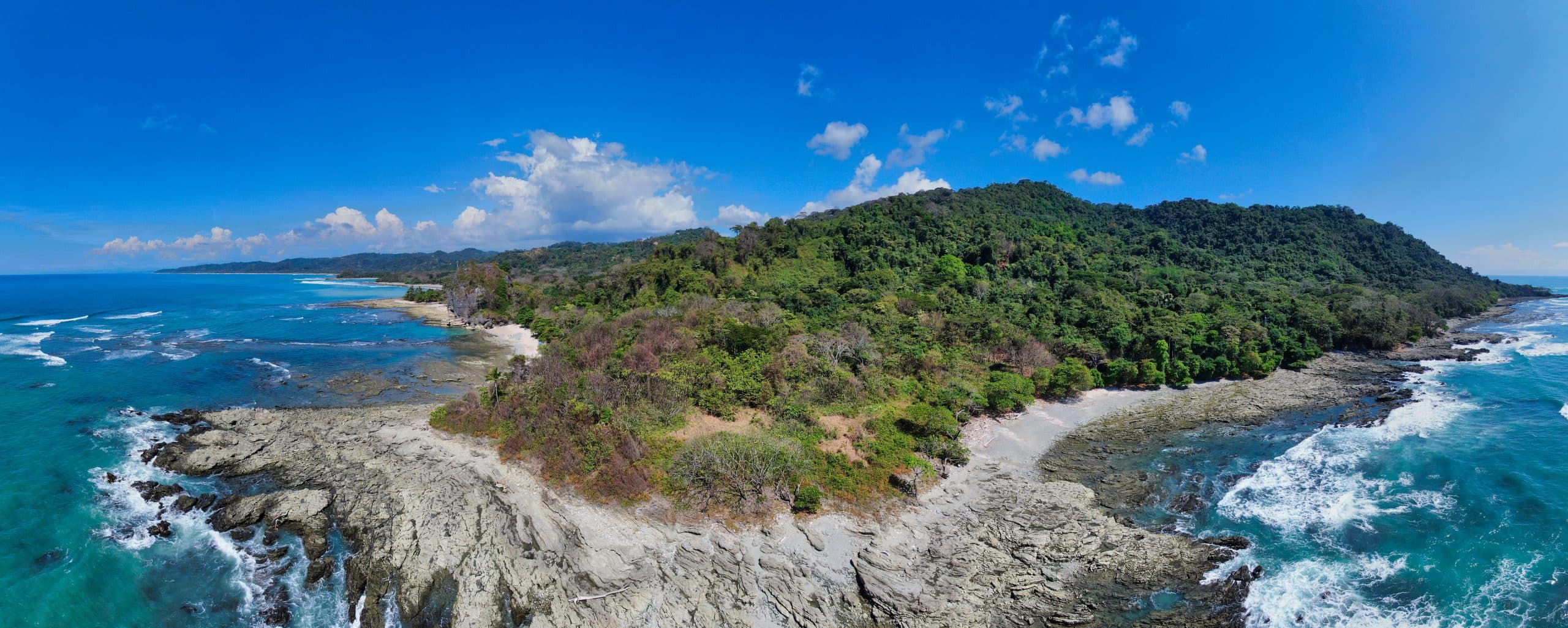 Aerial view of a lush green island surrounded by turquoise waters and rocky shores under a clear blue sky.