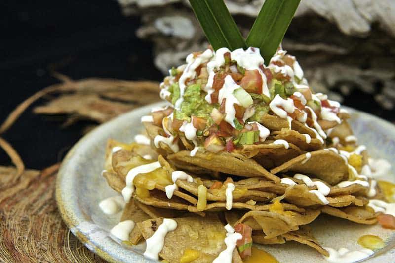 A plate of stacked nachos topped with guacamole, pico de gallo, and drizzled with crema.