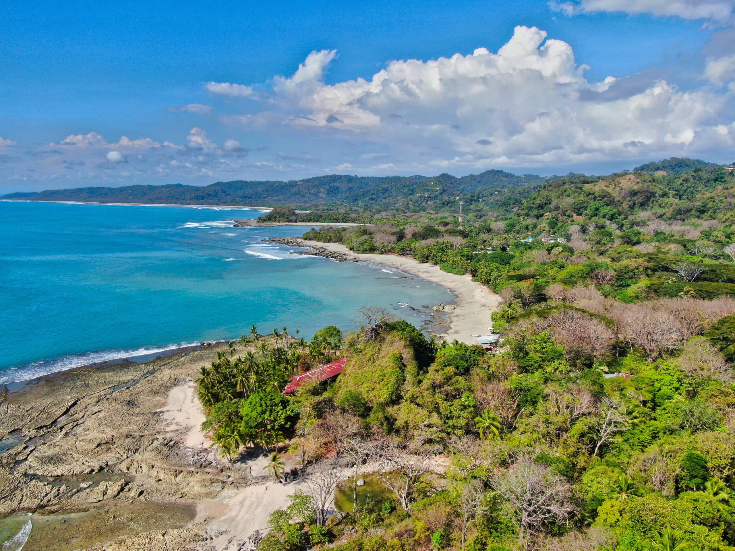Aerial view of a serene coastline with lush greenery and rocky shores under a bright blue sky.