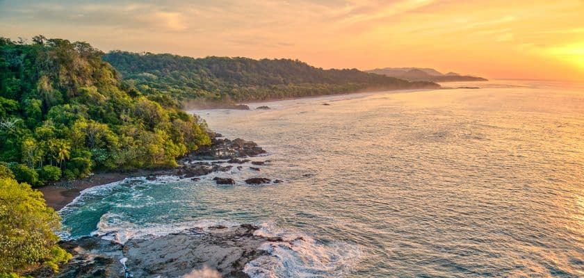 A breathtaking sunset over a tranquil ocean, with lush green cliffs and rocky shores.