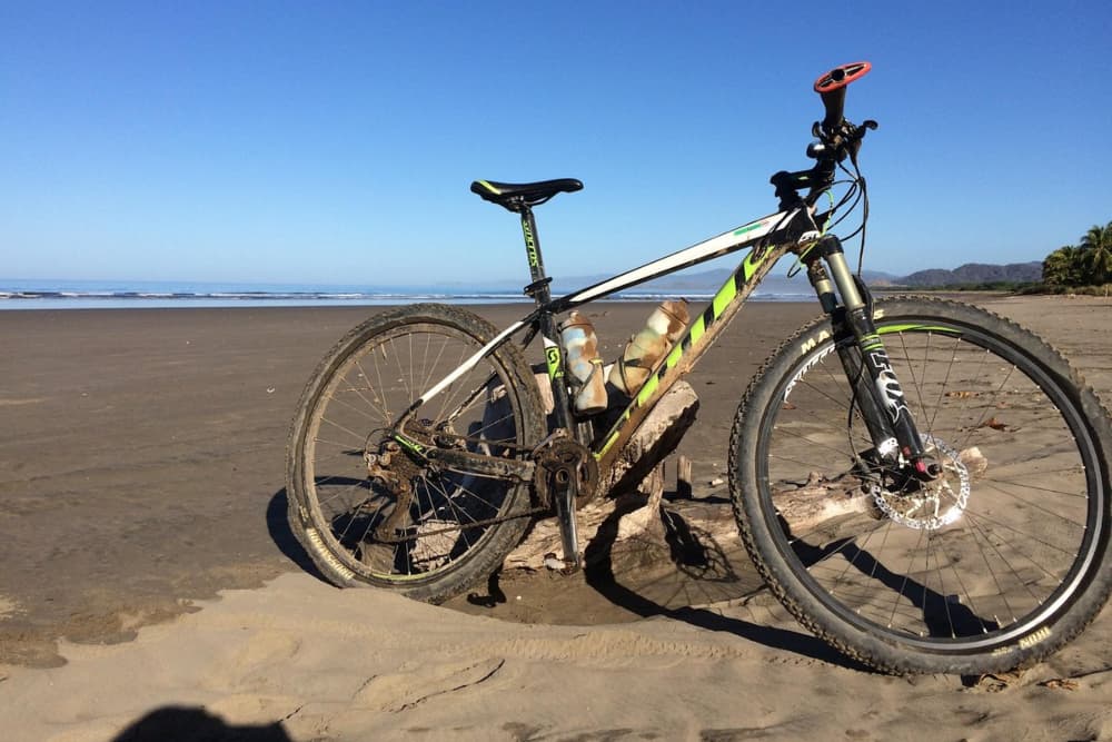 A white, black, and yellow mountain bike on the beach with the ocean in the background