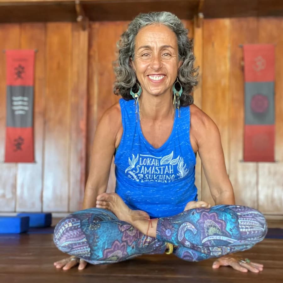 Smiling woman sitting in a cross-legged position while holding her body up off the ground with hands flat on the floor