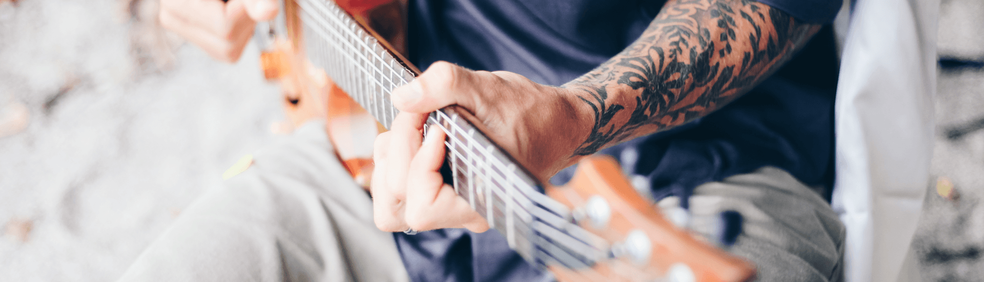 Man with tattoos, sitting playing guitar in blue shirt
