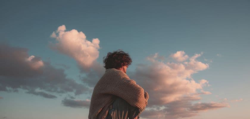 A person in a cozy sweater gazes at a colorful sky filled with clouds.