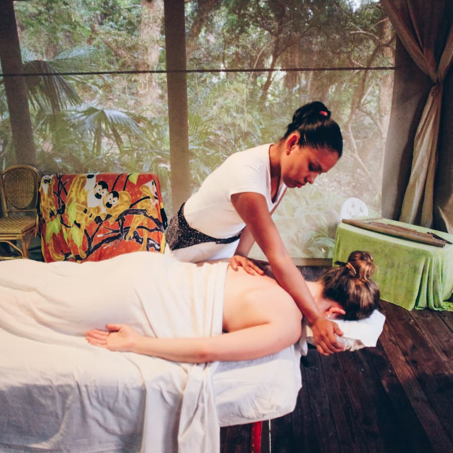 A woman having her back massaged by another woman in a jungle cabana