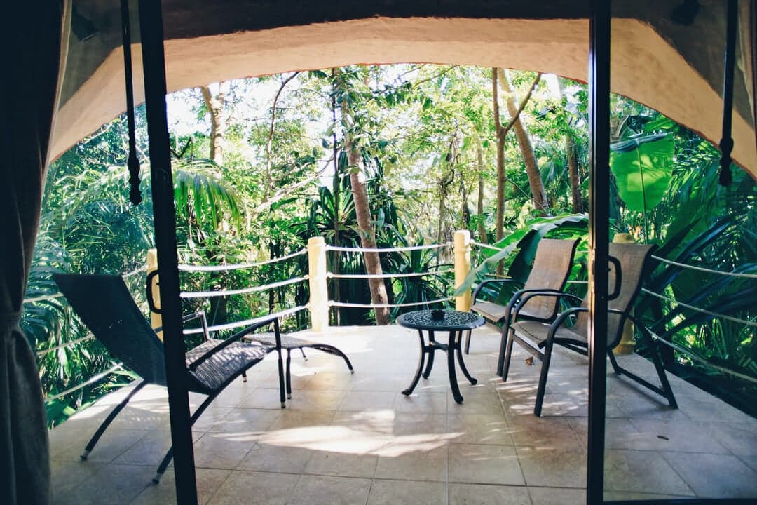 A cozy outdoor patio with chairs and a table surrounded by lush greenery.