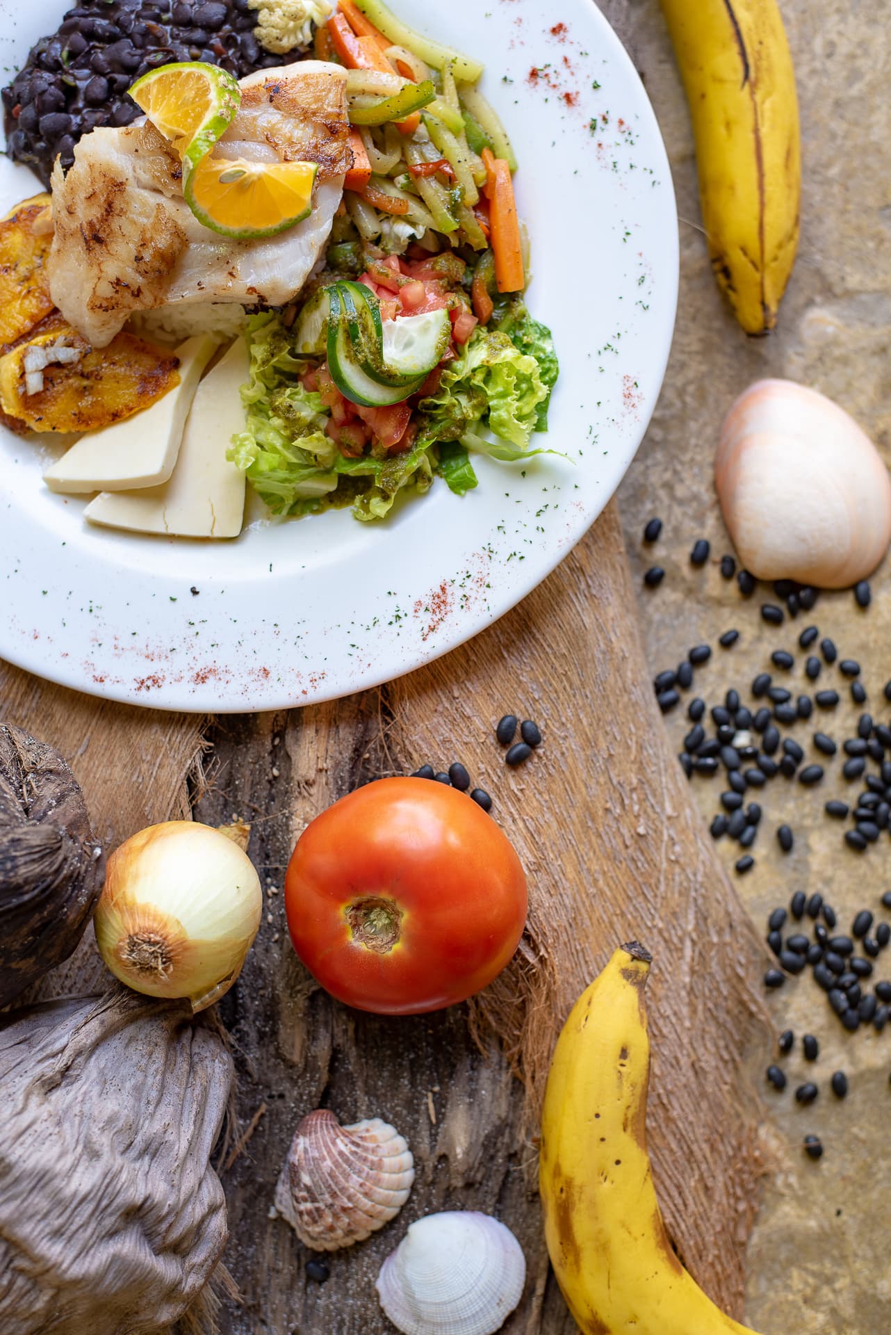 White plate on table with black beans, seafood, cheese and vegetables