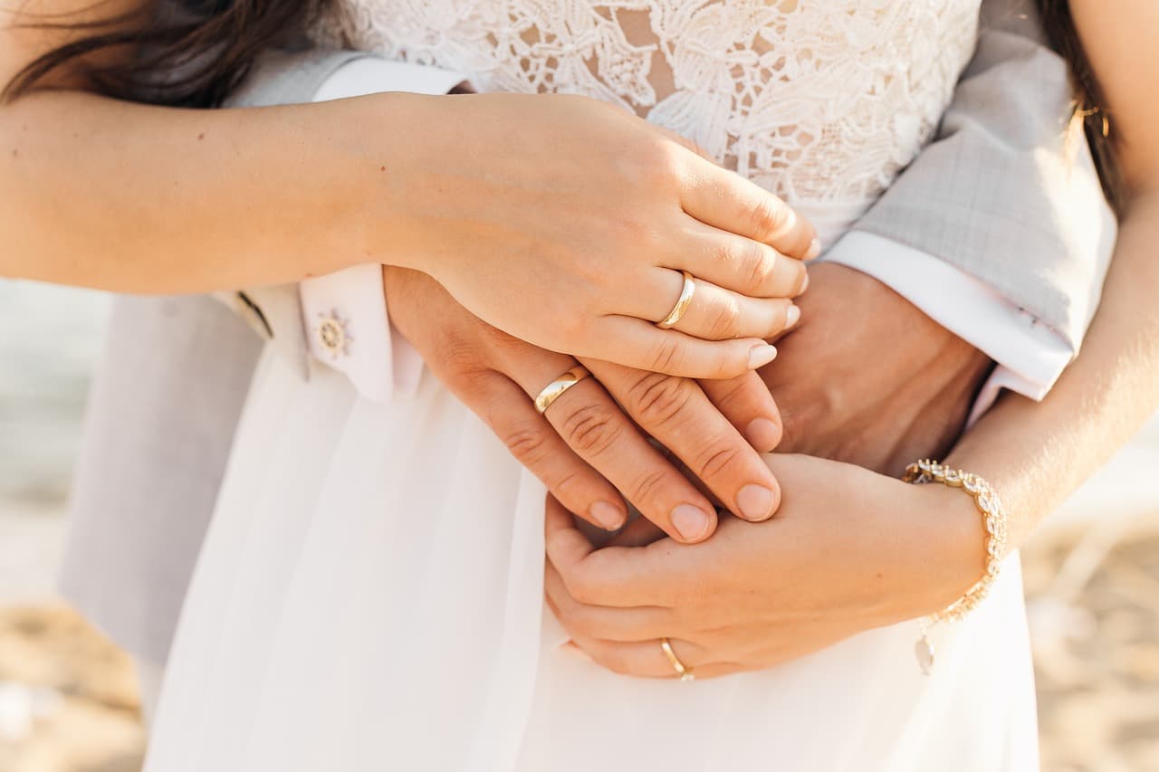 A close-up of entwined hands wearing wedding rings, symbolizing love and unity.