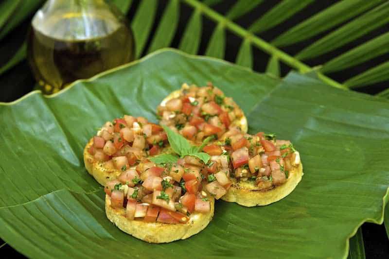 Three toasted rounds topped with a fresh tomato and herb mixture on a green banana leaf.
