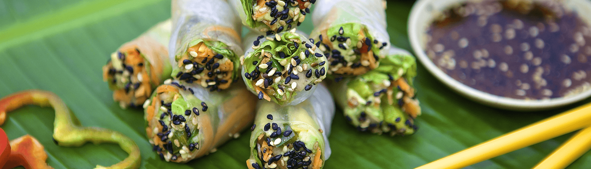 Green background with rice paper wrapped vegetable rolls with sesame seeds