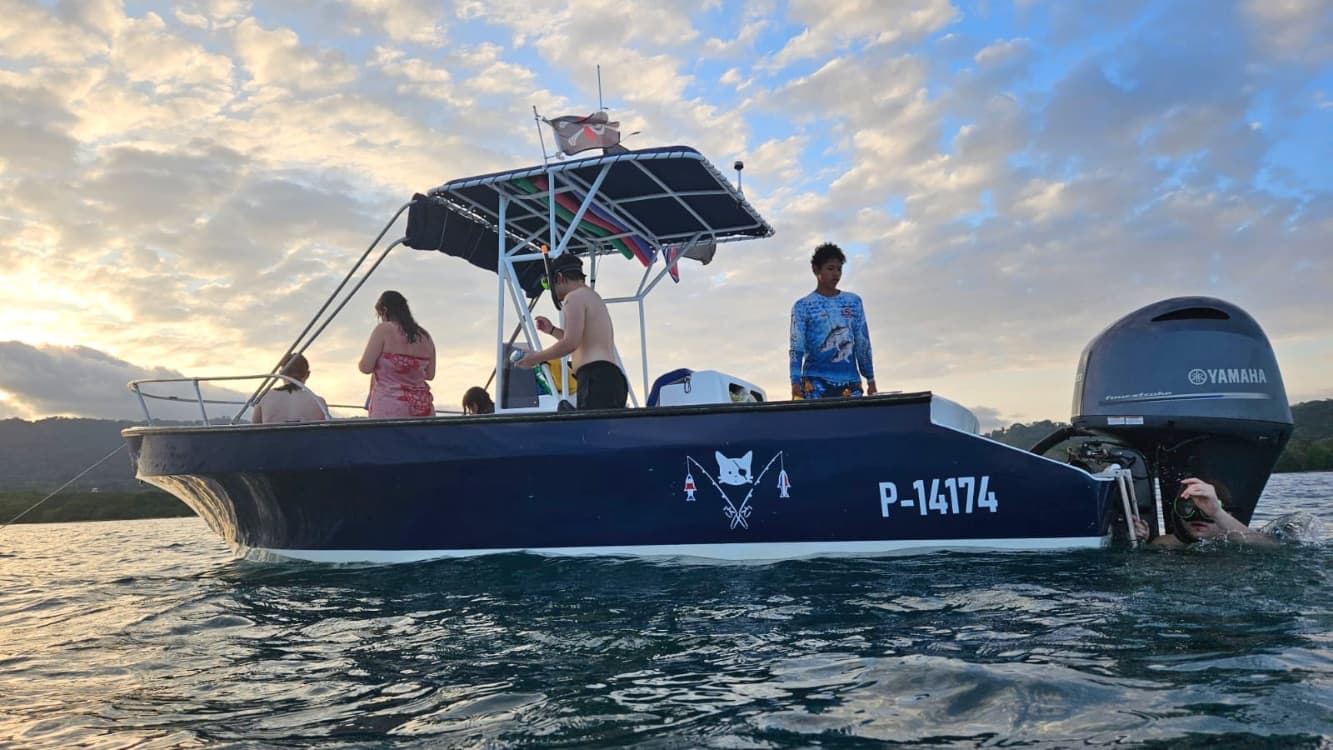 A group of people on a boat, with a motor and sunset in the background.