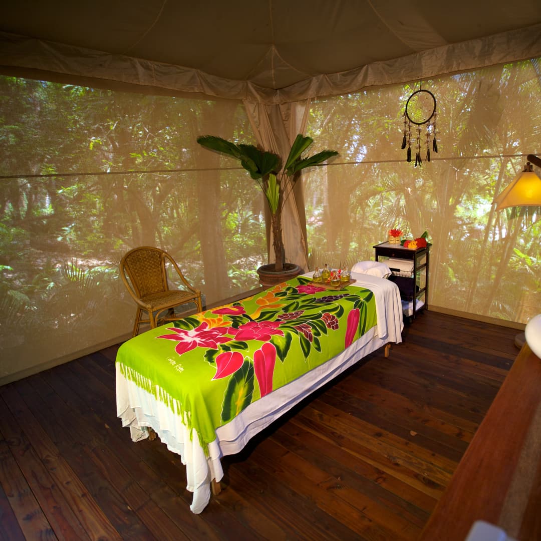 Massage table draped in colorful tropical-printed sheets set up in a screen-in jungle cabana with hardwood floors