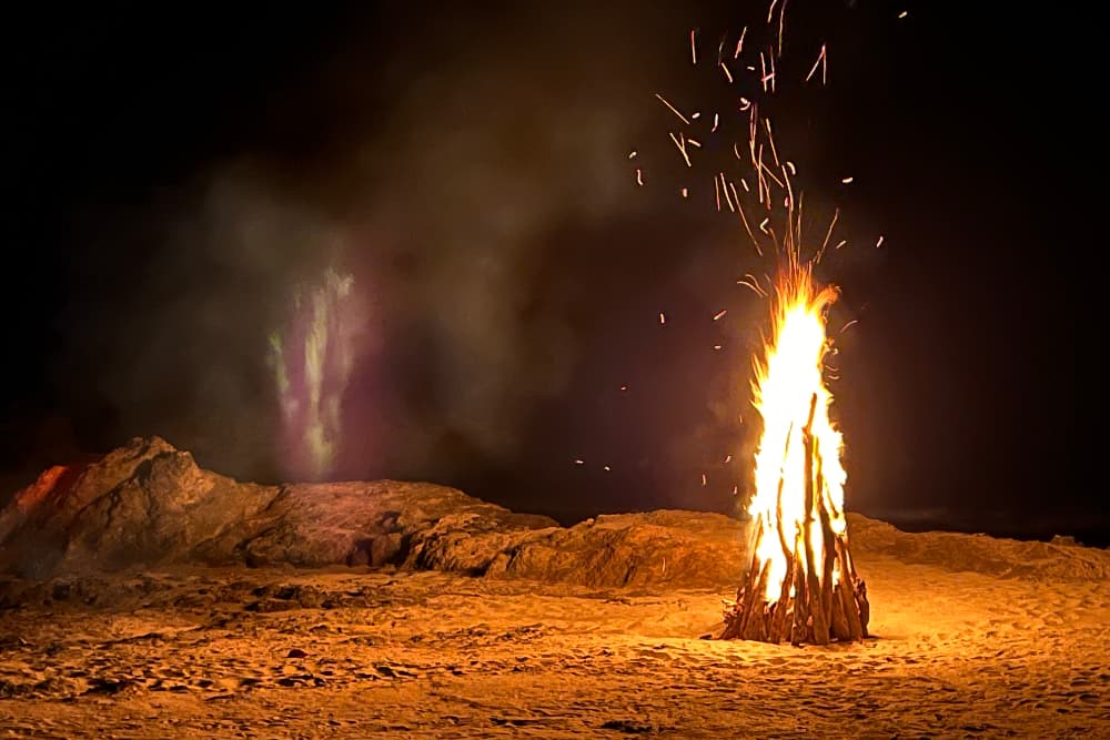 A bonfire at night on a sandy beach