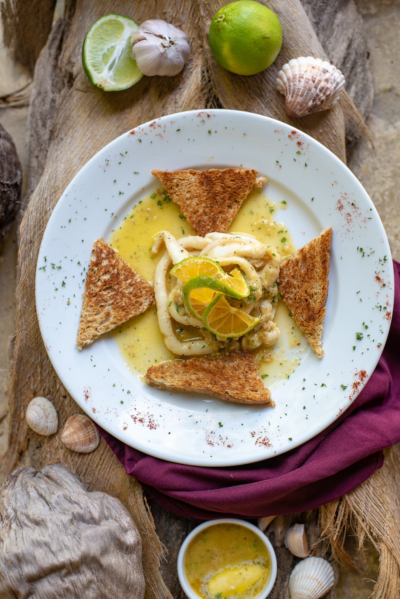 white plate with seafood in center and toast points with limes and shells on wood table