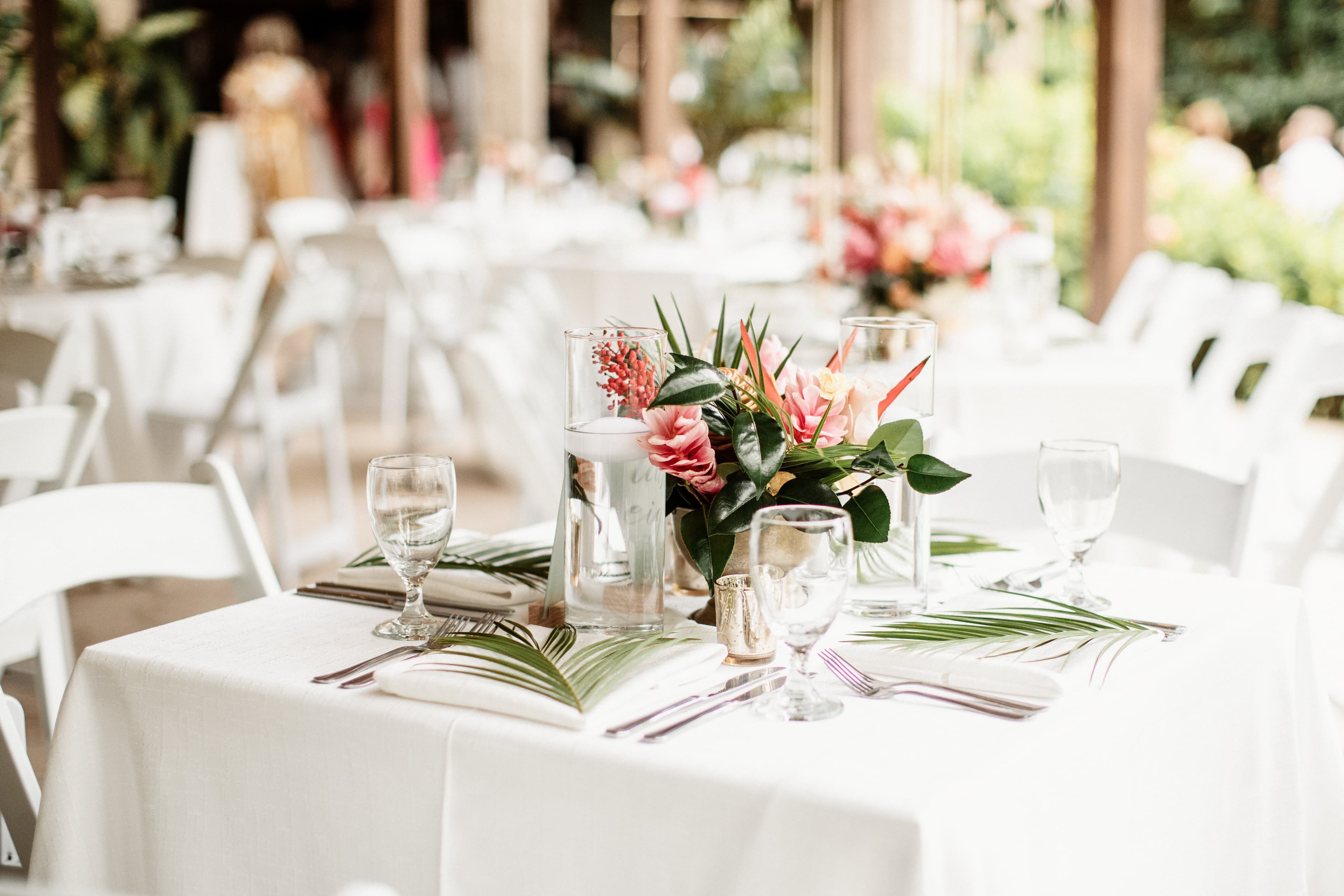 Close up of a table decorated for a wedding reception with a white tablecloth, tropical floral centerpiece, and clear water glasses