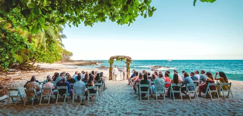 beach wedding ceremony in costa rica with guests seated under tropical trees facing the ocean at ylang ylang beach resort